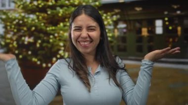 Açık mavi tişörtlü, sokakta yüzünü çerçeveleyen ve elleri açık dans eden İspanyol genç bir kadın..