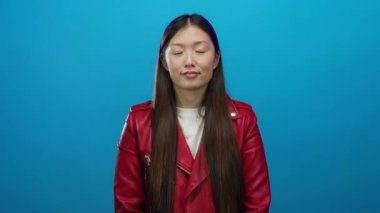 Kırmızı ceketli kadın mavi arka planda, gözleri kapalı sakin ve sakin bir şekilde izole bir ortamda.