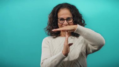 Kıvırcık saçlı bir kadın mavi arka planda, gözlük ve süveter takıp düşünceli ve anlamlı bir şekilde duraklama ya da kırılma kavramını temsil eden bir jest yapıyor..