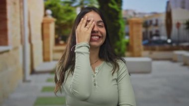 Uzun siyah saçlı genç İspanyol kadın parlak güneş ışığı altında dar taş caddede eli ile göz kaplıyor..