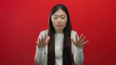 Sakince kırmızı arka plana karşı hareket eden, sükuneti vurgulayan, beyaz giyimli, izole edilmiş Asyalı kadın, barışçıl bir mesaj veriyor, sakin bir iletişim öneriyor..