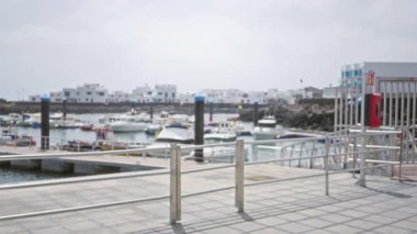 Bulanık binalar ve mavi gökyüzü arkaplanına kenetlenmiş yatları olan Marina, Bokeh etkisindeki dağılmış bir sahneyi gösteriyor, marinanın huzurlu ve pitoresk ortamını vurguluyor.