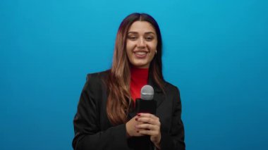İspanyol kadın muhabir canlı mavi bir arka plana karşı elinde bir mikrofon tutarken özgüvenle gülümsüyor, yayıncılıktaki profesyonellik ve coşkuyu somutlaştırıyor..