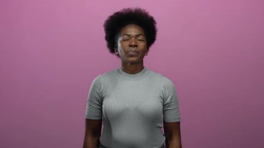 Huzurlu bir anın tadını çıkaran kadın pembe arka planda gözleri kapalı durarak sakin bir ifade sergiliyor..