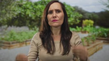 Güneşli bir günde canlı bir yeşil park ortamında hayal kırıklığını ifade eden bir kadın, yemyeşil yeşilliklerle çevrili, duygularını ve açık hava ortamını vurgulayan..