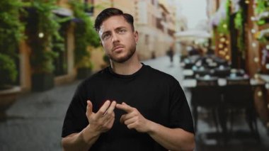 Sakallı genç adam bir şehir restoranının terasında parmaklarını sayıyor. Etrafı bitki ve sandalyelerle çevrili..