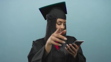 Şapkalı ve cüppeli İspanyol bir kadın, izole edilmiş mavi bir arka plana karşı Suudi pasaportu taşıyor. Bu da bir yolculuk ya da yeni bir başlangıç olduğunu gösteriyor..