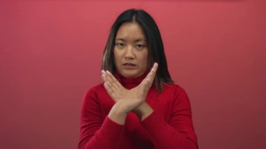 Çapraz kollu genç bir kadın canlı kırmızı bir zemin üzerinde duruyor, etkileyici duruşu ve ciddi ifadesi ile direnç ve başkaldırı hissini iletiyor..