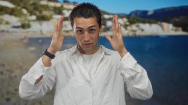 Beyaz gömlekli genç İspanyol adam deniz kenarı manzaralı güneşli sahil sahilinde elleri başının üstünde yaratıcı vizyon.