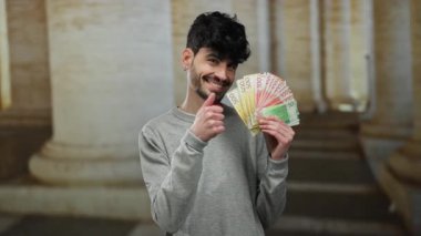 Norveçli Krone 'u elinde tutan adam eski bir üniversitede açık havada para yatırıyor, akademik bir ortamda kendine güvenen bir ifadeyle para gösteriyor..