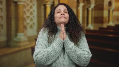Kilisede dua eden kadın rahat bir kazak giyiyor. Yüzü, huzurlu iç mimari tarafından çevrelenmiş kutsal bağlılığı yansıtıyor..