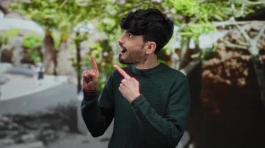 Parkta coşkuyla gülümseyen genç bir adam, yemyeşil yapraklarıyla, parlak güneşli bir günde yukarıya doğru bakıyor..