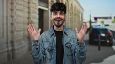 Kot ceket giyen genç adam, coşkulu bir şekilde gülümsüyor ve şehrin hareketli sokaklarında elleri havada geziyor..