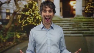 Ağzı açık ve kolları açık bir adam sokakta aydınlanmış ağaçların ve alacakaranlıkta taş basamakların yanında; heyecan.