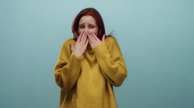 Sarı kazaklı kızıl saçlı bir kadın mavi bir duvara karşı utangaç bir şekilde poz veriyor, stok medyasında yaratıcı kullanım için izole bir ortamda güzellik ve duyguyu vurguluyor..