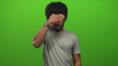 Yüzü ve ağzı yeşil arka planda olan adam duygularını ve ifadesini sakal, saat ve günlük kıyafetlerle ifade ediyor..