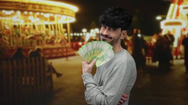 Rus rublesi banknotları olan bir adam açık hava fuarında gülümsüyor, arka planda canlı ışıklar ve atlı karınca var, neşeli ve neşeli bir anı yakalıyor..
