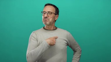 Yeşil arka planda izole edilmiş gözlük takan İspanyol olgun bir adam kendini sert bir ifadeyle gösteriyor..