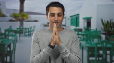 Gri kazaklı genç adam güneşli bir terasta birlikte gülümsüyor yeşil sandalyeleri ve masaları olan parlak bir restoran ortamının arka planında.