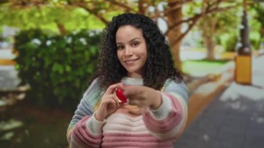 Parktaki İspanyol kadın bana jest yaparken gülümsüyor ve açık havada canlı yeşil ağaçların altında kırmızı bir kalp sembolü tutuyor..