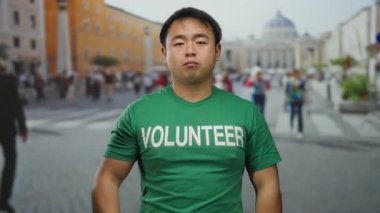 Yeşil gönüllü tişörtlü Asyalı adam St. Peter Meydanı, Vatikan 'da, insanların bulanık geçmişi ve tarihi mimarisi ile selamlıyor..