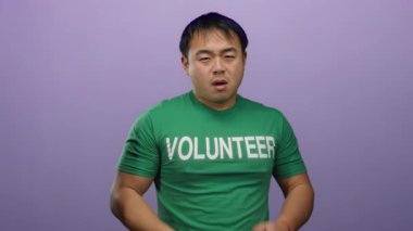 Yeşil gönüllü gömlekli genç adam mor arka planda şakacı hareketler yapıyor.