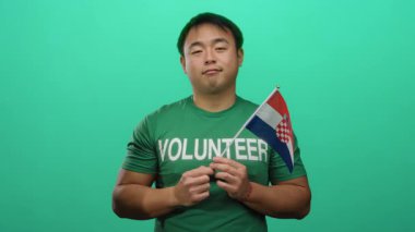 Genç adam, gönüllü gömleği giyerken yeşil arka planda bir Hırvat bayrağı tutuyor..