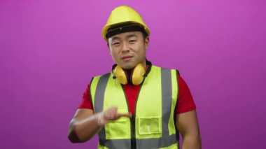 Güvenlik teçhizatı takan inşaat işçisi canlı pembe bir arka plana karşı bağırıyor, enerji ve komutu ifade ediyor.