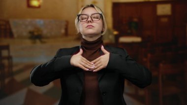 Huzurlu kilise ortamında meditasyon yapan bir kadın, odaklanmış ve sakin bir ifade sergiliyor, şık giyinmiş, ruhani sükuneti ve tefekkürü ön plana çıkarıyor..