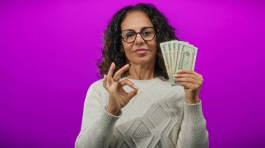 Gözlüklü kadın, canlı mor bir arka plana karşı iyi bir jest yaparak bize dolar veriyor, kendine güven ve başarı gösteriyor..