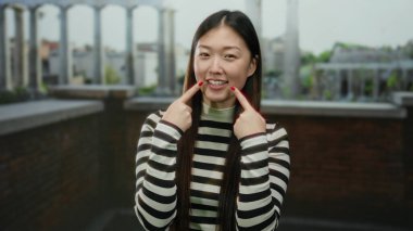 Roma harabelerinde çizgili gömlek giymiş, arka planda antik mimari olan bir kadın şehir ortamında parlak bir gün ışığında neşeli bir ifade ve gündelik bir tarz sergiliyor..