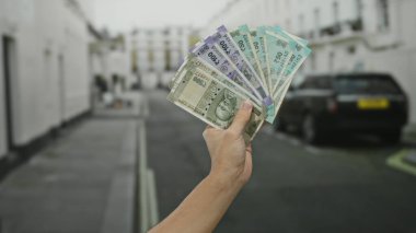 Kafkasyalı bir adam, şehir sokaklarında Hindistan parası tutuyor, para, finans ve ekonomi unsurlarını modern şehir ortamında sergiliyor..