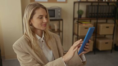 Kadın ofiste otururken selfie çekiyor. Arka planda raflı bej ceket ve mikrodalga fırın var. Günlük iş ortamını gösteriyor..