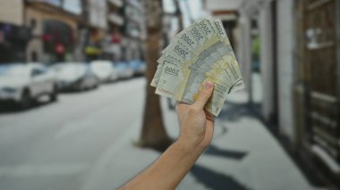 Bir şehir caddesinde Endonezya rupia banknotları tutan adam arka planda bulanık arabalarla açık bir şehir ortamında para gösteriyor..