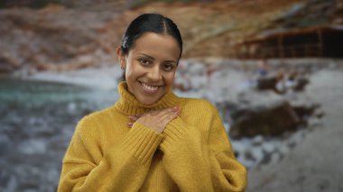 Yüzü kapalı, elleri göğsünde gülümseyen, deniz kenarında sarı bir kazak giyen, bulanık bir plaj geçmişi olan bir kadın, minnettarlık ve sükunet hissi veriyor..