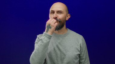 Sakallı kel adam mavi arka planda jest yapıyor gri süveter giyiyor cazibesi ve kendine güveni var..