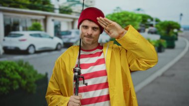 Sarı yağmurluklu ve kırmızı bereli genç adam şehir sokaklarında oltayla selamlıyor. Açık hava cazibesini somutlaştırıyor..