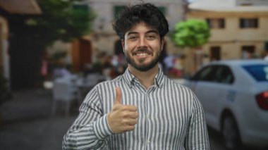 Çizgili tişörtlü, sakallı genç adam güneşli caddede arabalarla gülümsüyor ve binaların arka planlarını bulanıklaştırıyor..