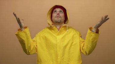 Kahverengi arka planda sarı yağmurluk giyen adam değişik ifadeler sergiliyor..