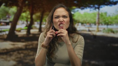 Yeşil bir park ortamında akıllı telefondan konuşan bir kadın, bağlantı ve iletişim odaklı genç doğa yaşam tarzını yakalıyor..