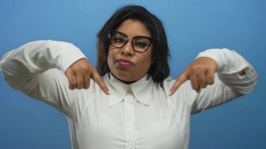 Kendinden emin bir ifadeyle aşağıya bakan, mavi arka planda gözlüklü ve beyaz gömlekli bir kadın, güçlendirilmiş bir Latin kimliği tasvir ediyor..