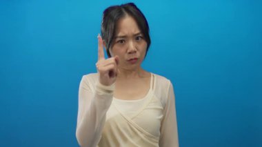 Genç Çinli kadın kendinden emin ifadeyi tasvir eden izole edilmiş mavi arka plan duvarını işaret ediyor..
