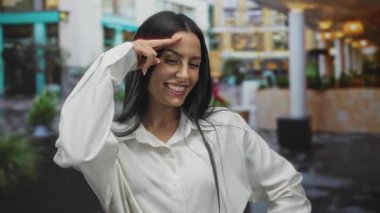 Açık havada gülümseyen genç bir İspanyol kadın elleri başının üstünde neşeli bir jest yapıyor, neşe ve kendine güveni ifade ediyor..