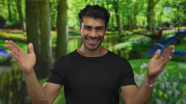 Uzun ağaçlarla çevrili yeşil ormanda büyük boy jest yaparak gülümseyen İspanyol genç adam; açık davet neşe karşılar.