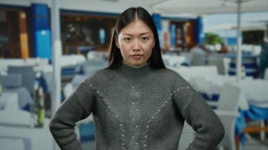 Kapalı gözlü bir kadın, şehir restoranının terasında dikiliyor. Açık havada gri bir kazak giyiyor ve yüzünde odaklanmış bir ifade var..