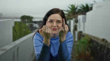 Mavi kazaklı kadın şehir sokağında, arka planda yeşillik ve açık havada moda ve kendine güvenen vücut dili ile etkileyici bir jest yapıyor..