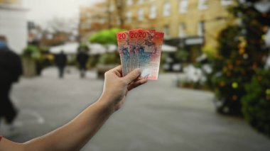 Kalabalık bir şehirde el ele tutuşan İsviçre frangı banknotları. Arka planda yürüyen insanlar açık havada finansal bir değiş tokuş öneriyor..