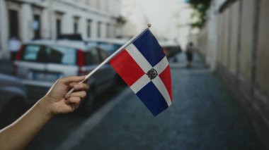 Dominik Cumhuriyeti bayrağını bir şehir caddesinde tutarak arka planda arabaları ve binaları olan hareketli bir şehir kasabasında canlı bir kültürel gurur yakaladılar..