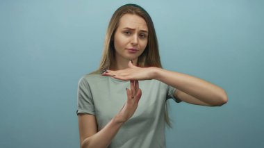 İzole edilmiş mavi duvarın önünde el kol hareketi yapan bir kadın izole edilmiş bir arka planda sarı saçlı, gündelik bir ifade sergiliyor..