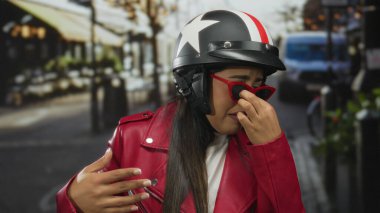 Kadın el ele tutuşup, dışarıda yüzünü buruştururken Latin Latin asıllı genç bisikletçi sokakta park etmiş motosiklet kaskını kavradı..